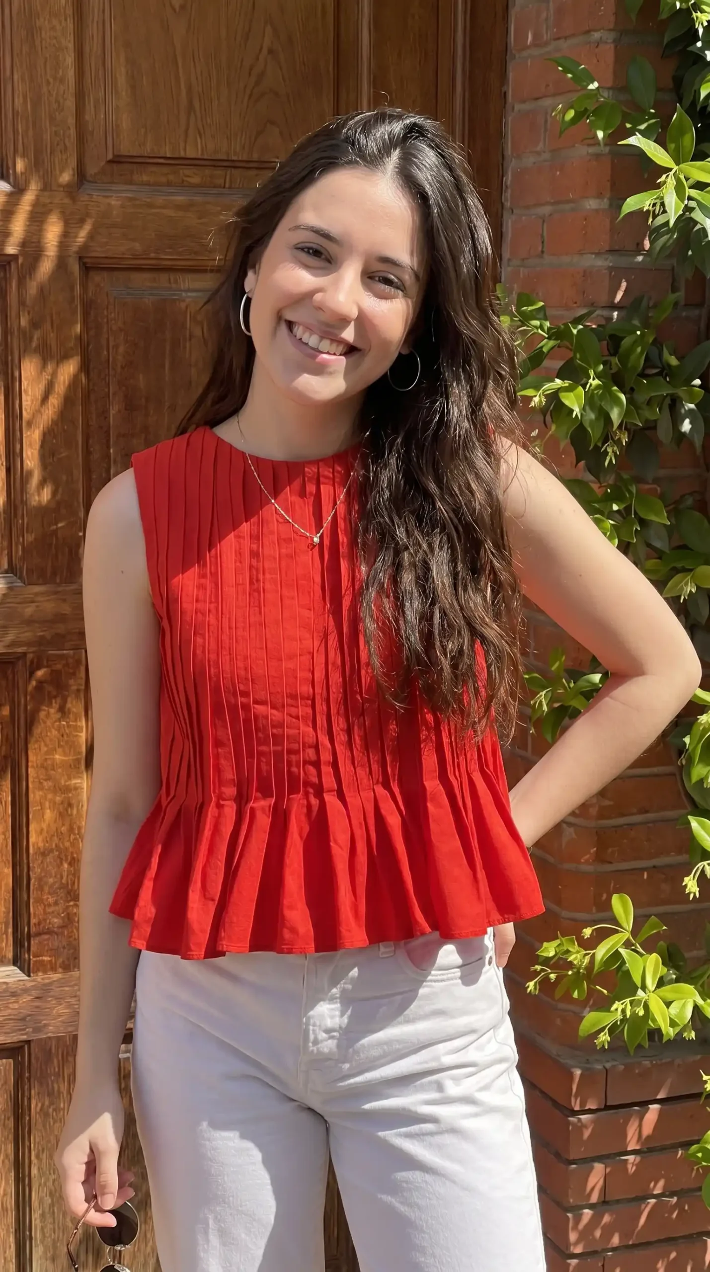Woman wearing red pleated sleeveless peplum top with white jeans outdoors in summer