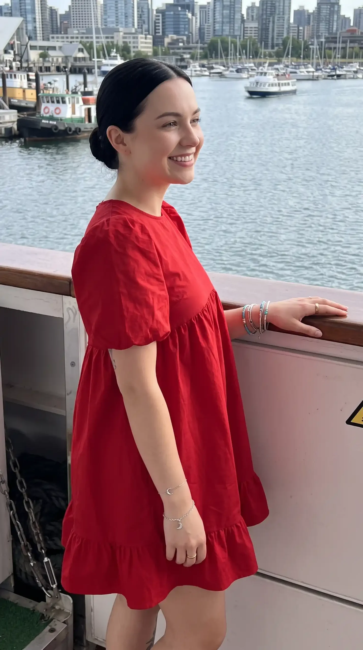 Woman wearing red puff sleeve round neck tiered babydoll mini dress with stacked bracelets at waterfront