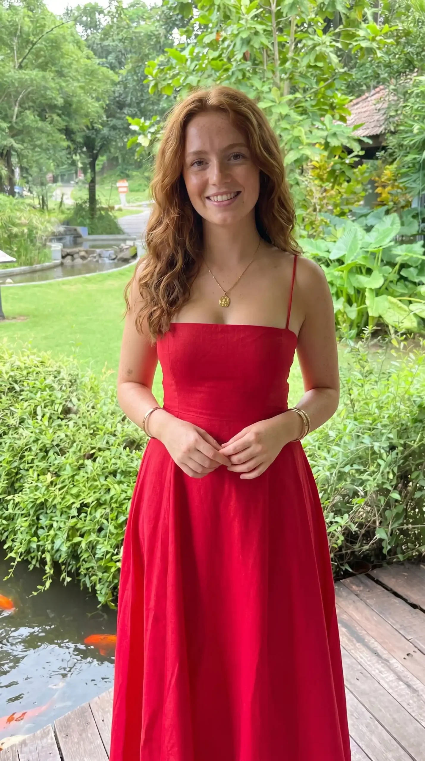 Woman wearing red spaghetti strap square neck linen maxi dress in tropical garden setting