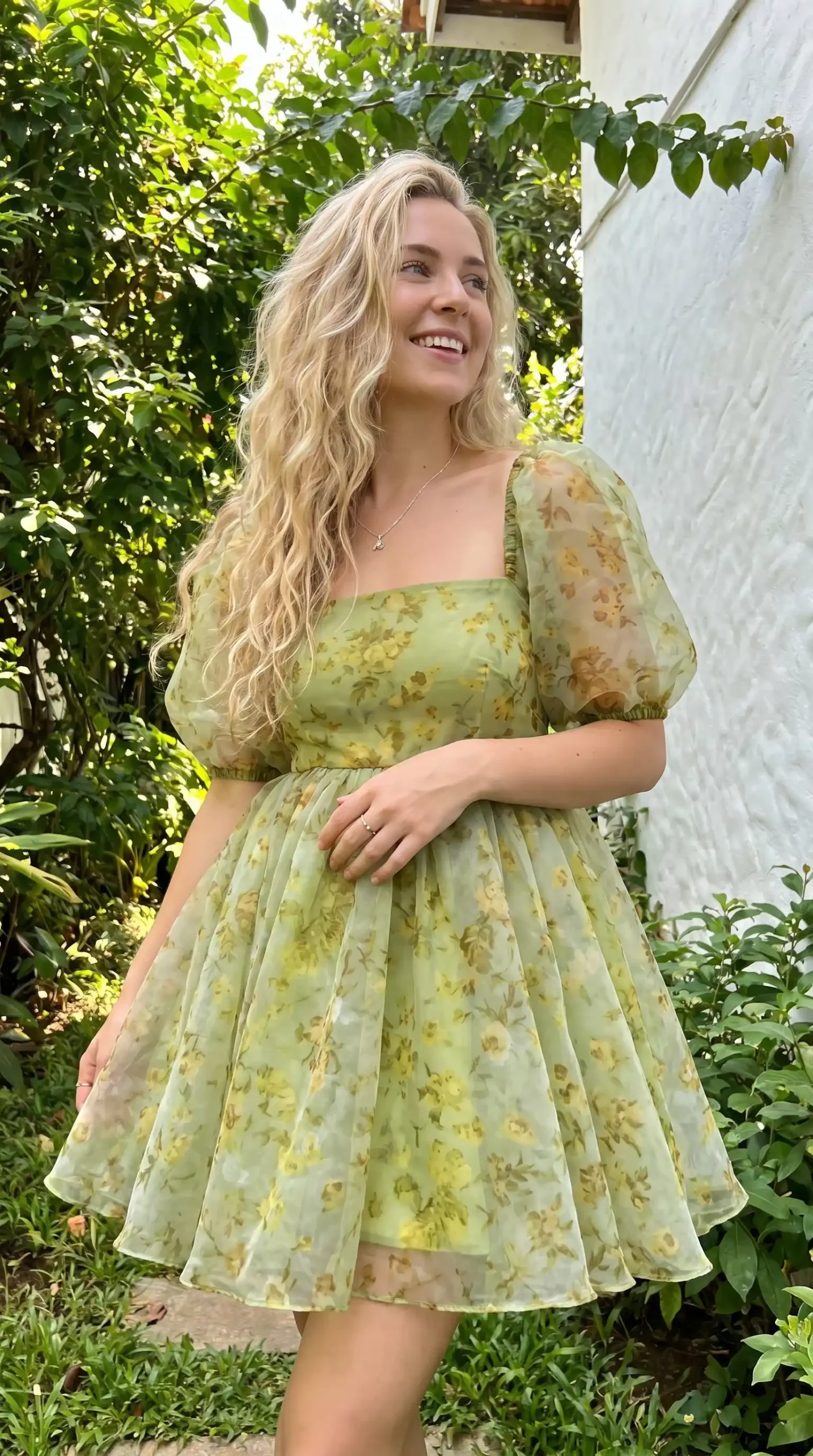 Woman wearing sage green floral organza puff sleeve square neck mini dress in garden in summer