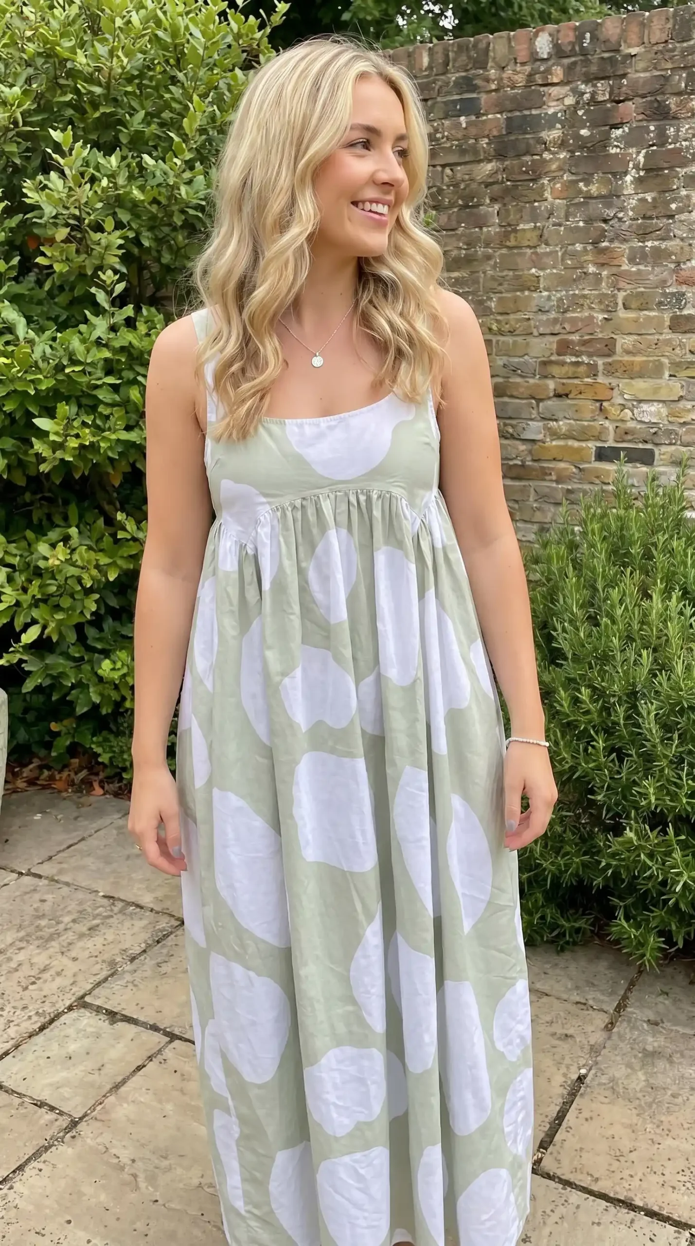 Woman wearing sage green and white oversized polka dot strappy maxi dress in garden in summer