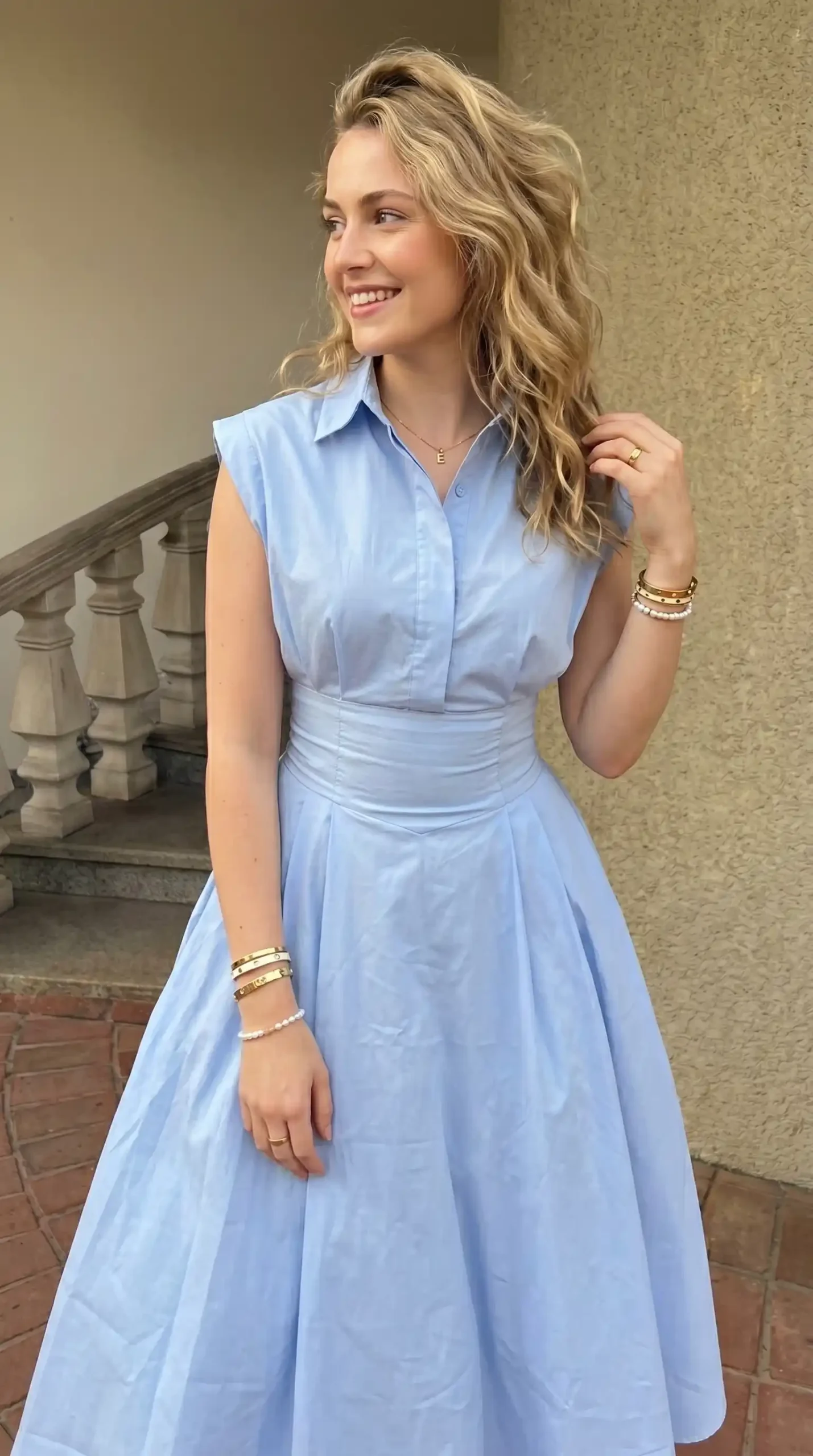 Woman wearing sky blue sleeveless collared A line midi dress with gold accessories outdoors