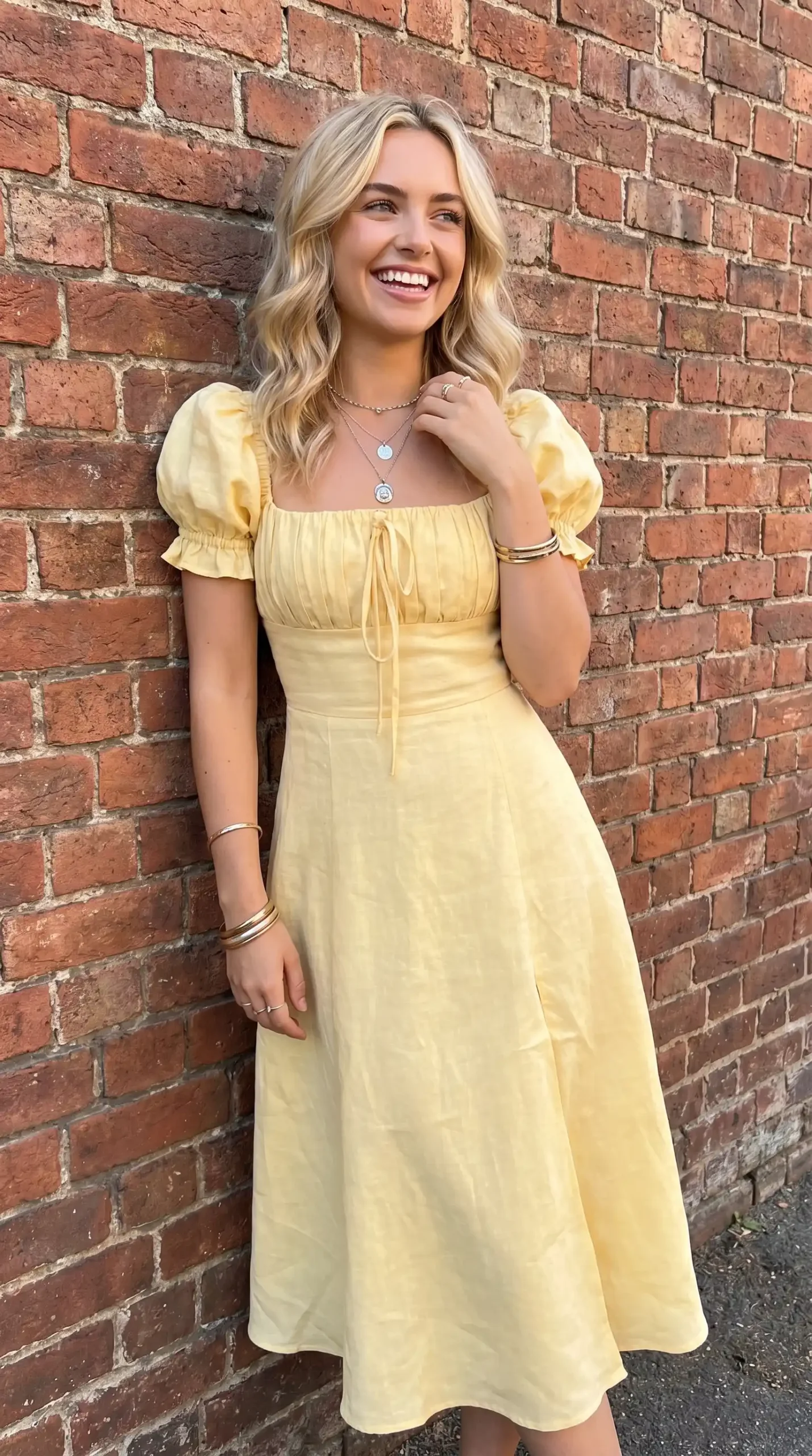Woman wearing soft yellow puff sleeve tie front square neck midi dress against brick wall in summer