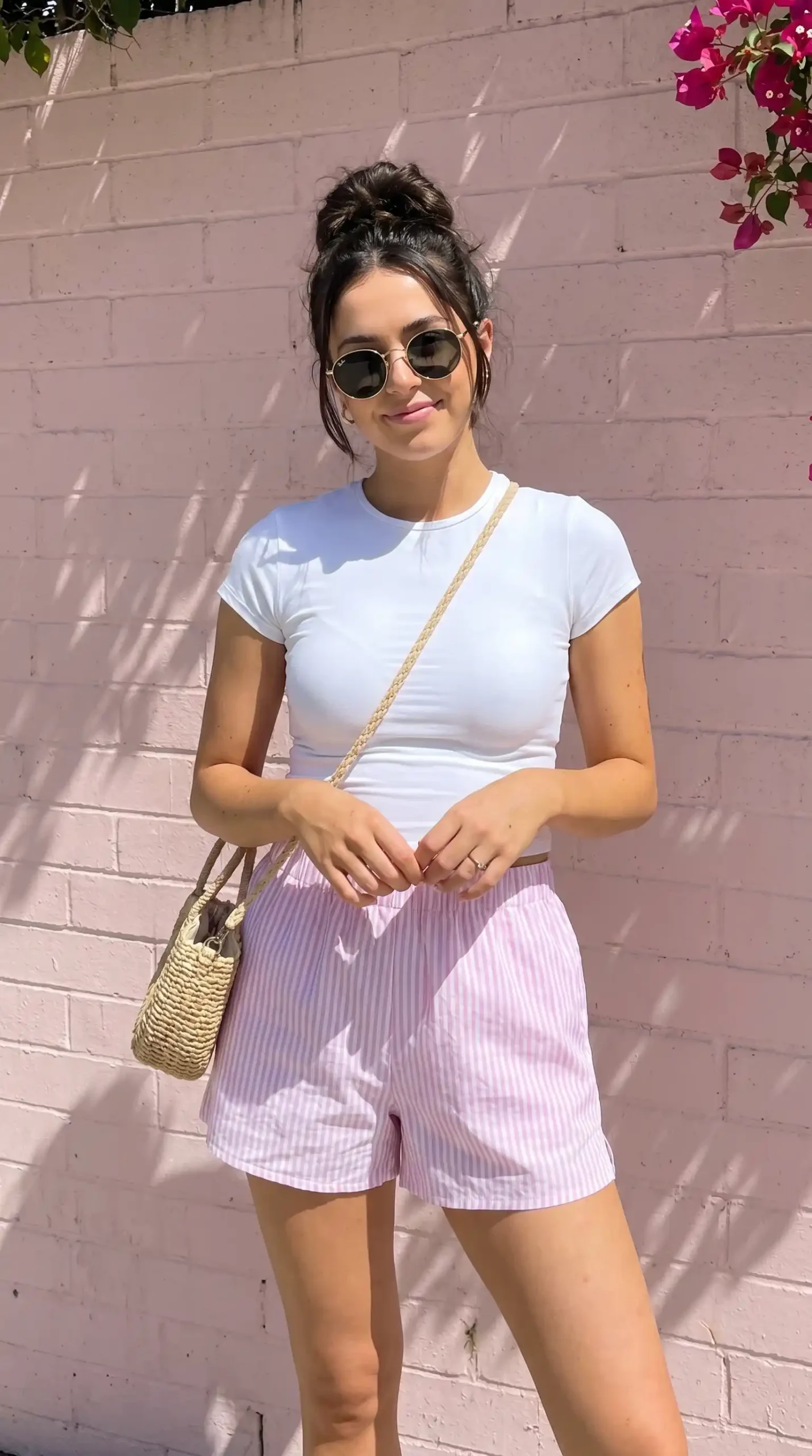 Woman wearing white crop tee with pink and white striped shorts and wicker crossbody bag outdoors