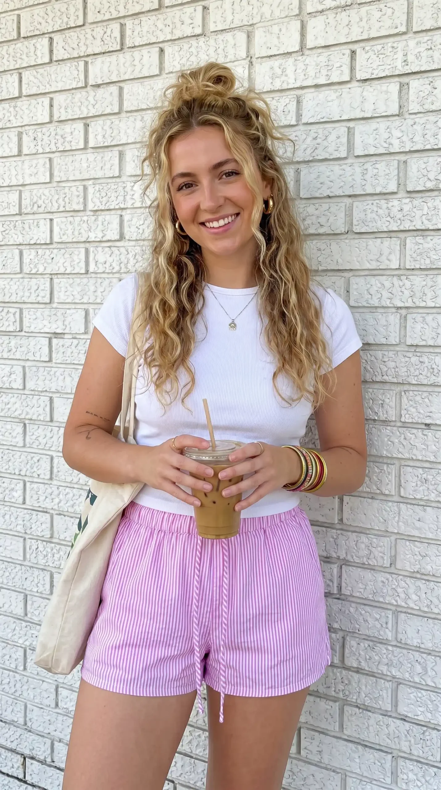 Woman wearing white ribbed crop tee with lilac pink striped drawstring shorts holding iced coffee outdoors