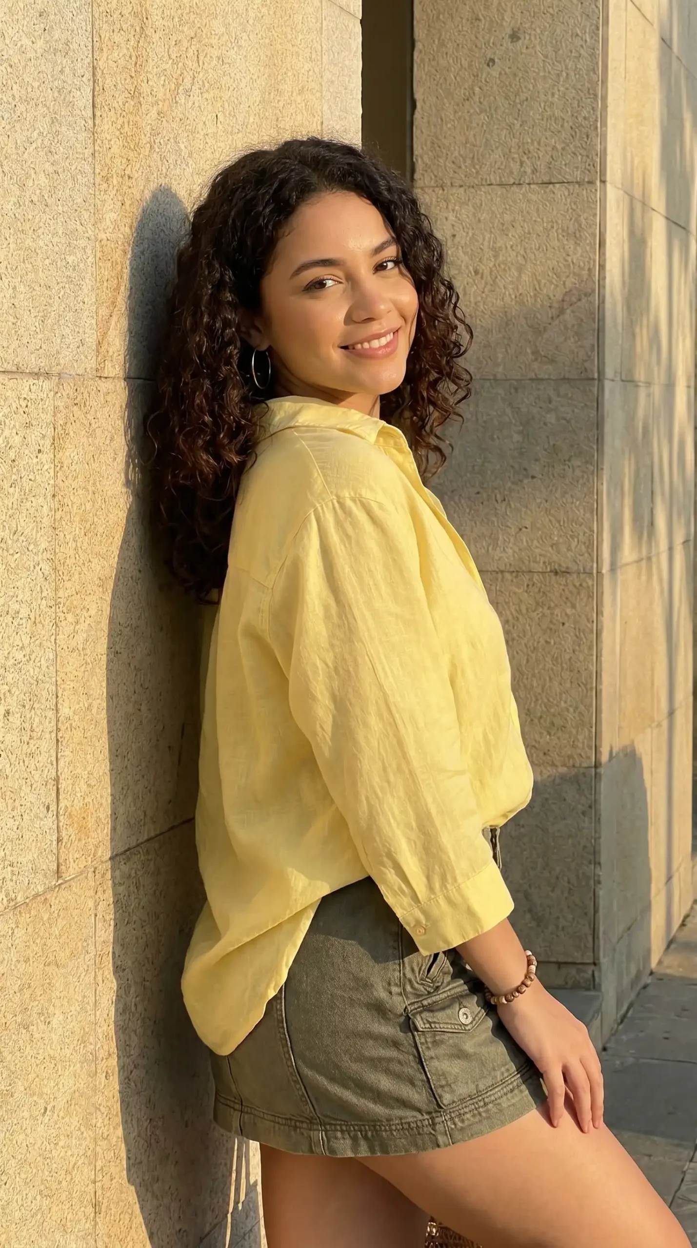 Woman wearing yellow button-up shirt with khaki denim mini skirt against stone wall