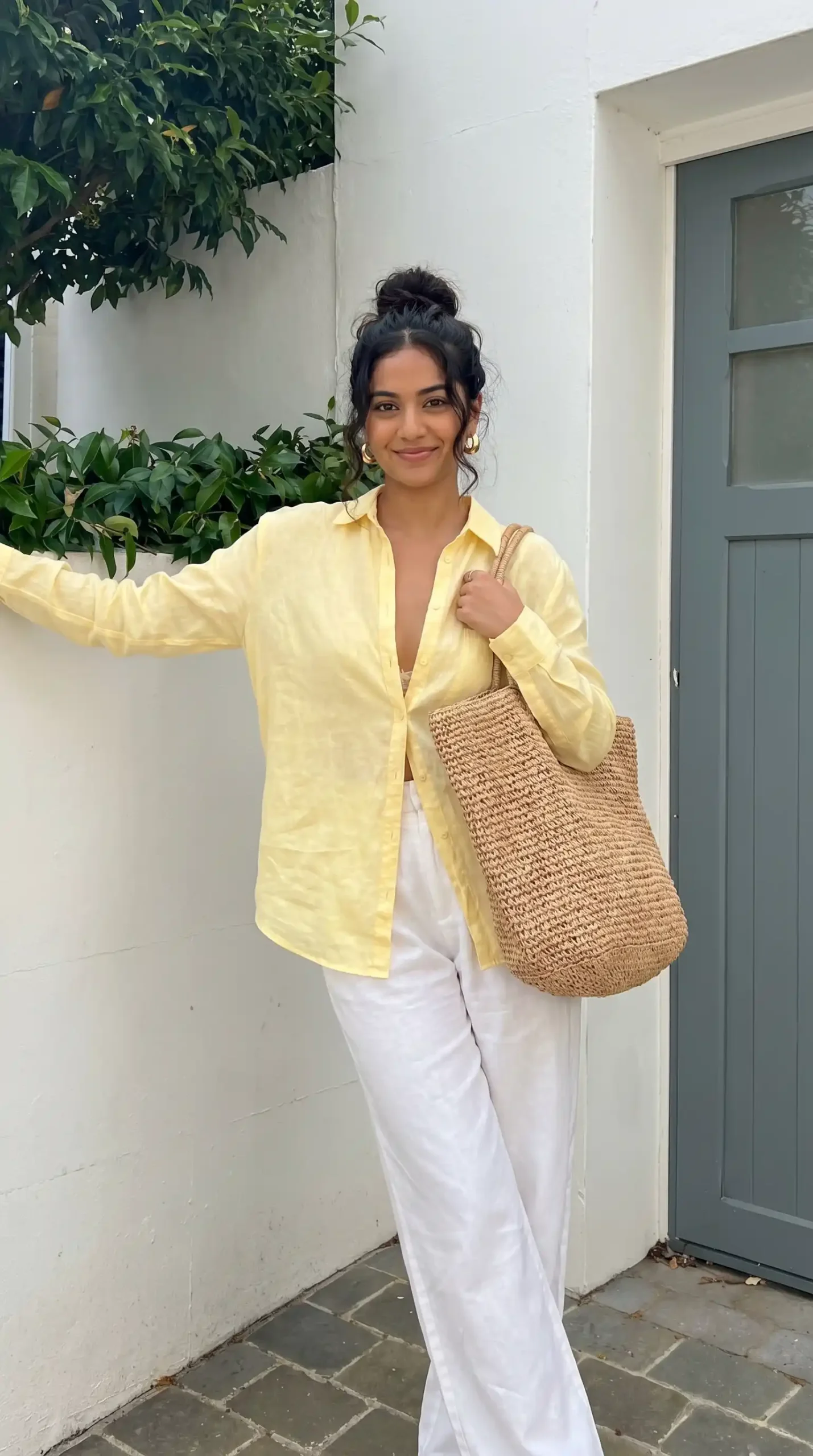 Woman wearing yellow button-up shirt with white wide leg pants and woven bag