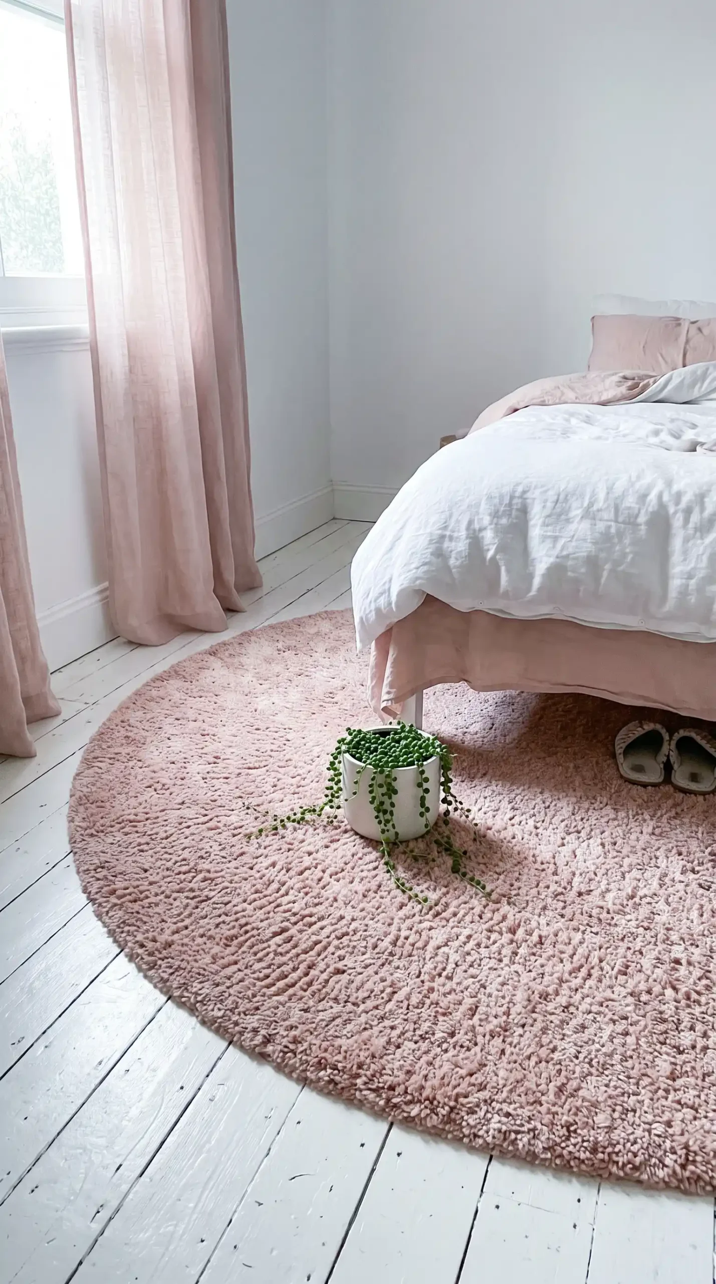Large round blush pink shaggy rug on white painted wood floor beside bed in feminine bedroom
