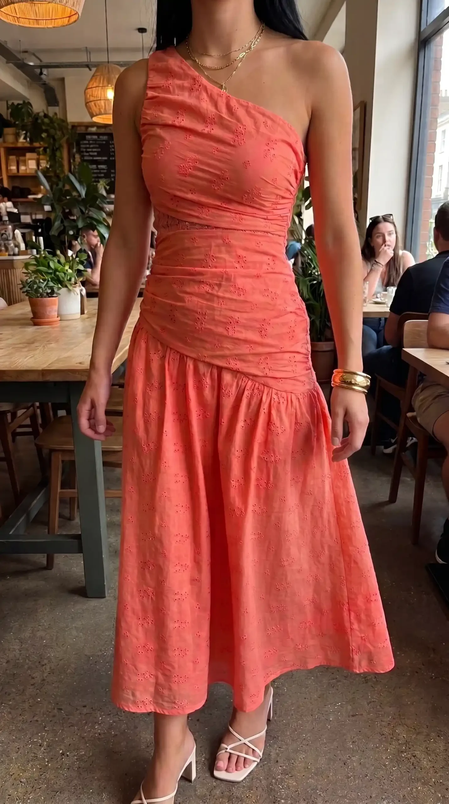 Woman wearing coral orange one shoulder eyelet ruched midi dress with white heels