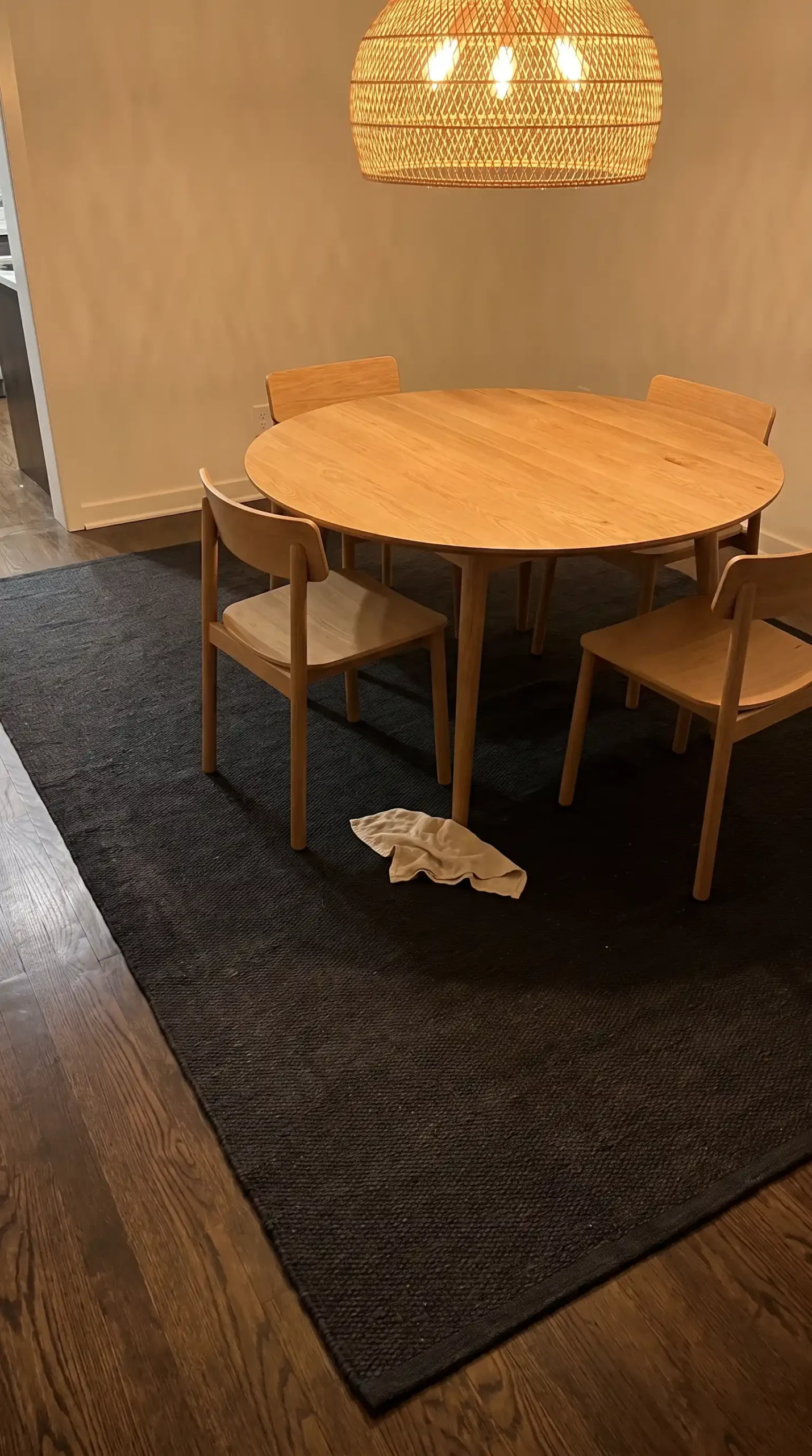 Large dark charcoal flatweave rug under round oak dining table with chairs in warm modern dining room