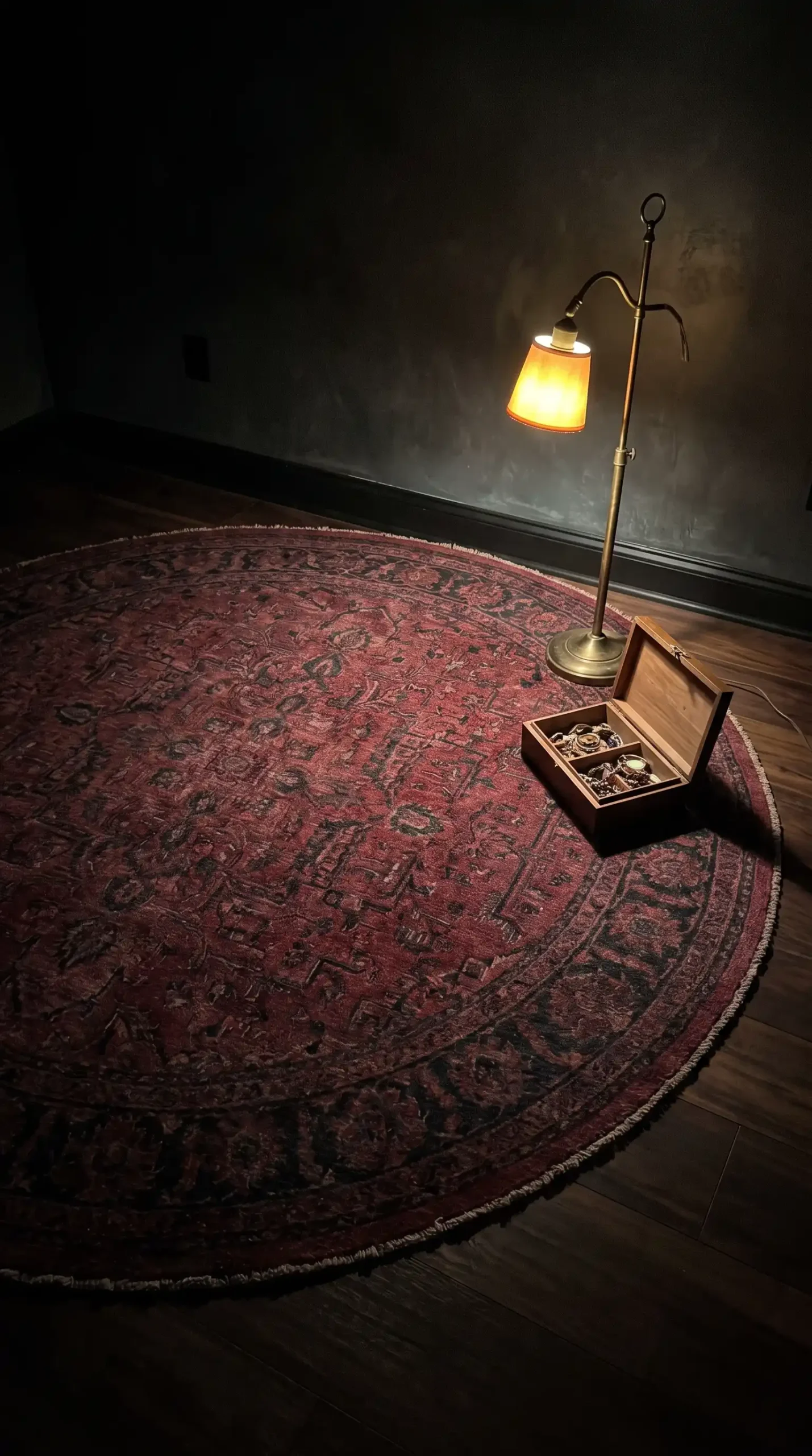 Large round deep burgundy and black hand knotted wool rug on dark walnut floor in moody bedroom with brass floor lamp