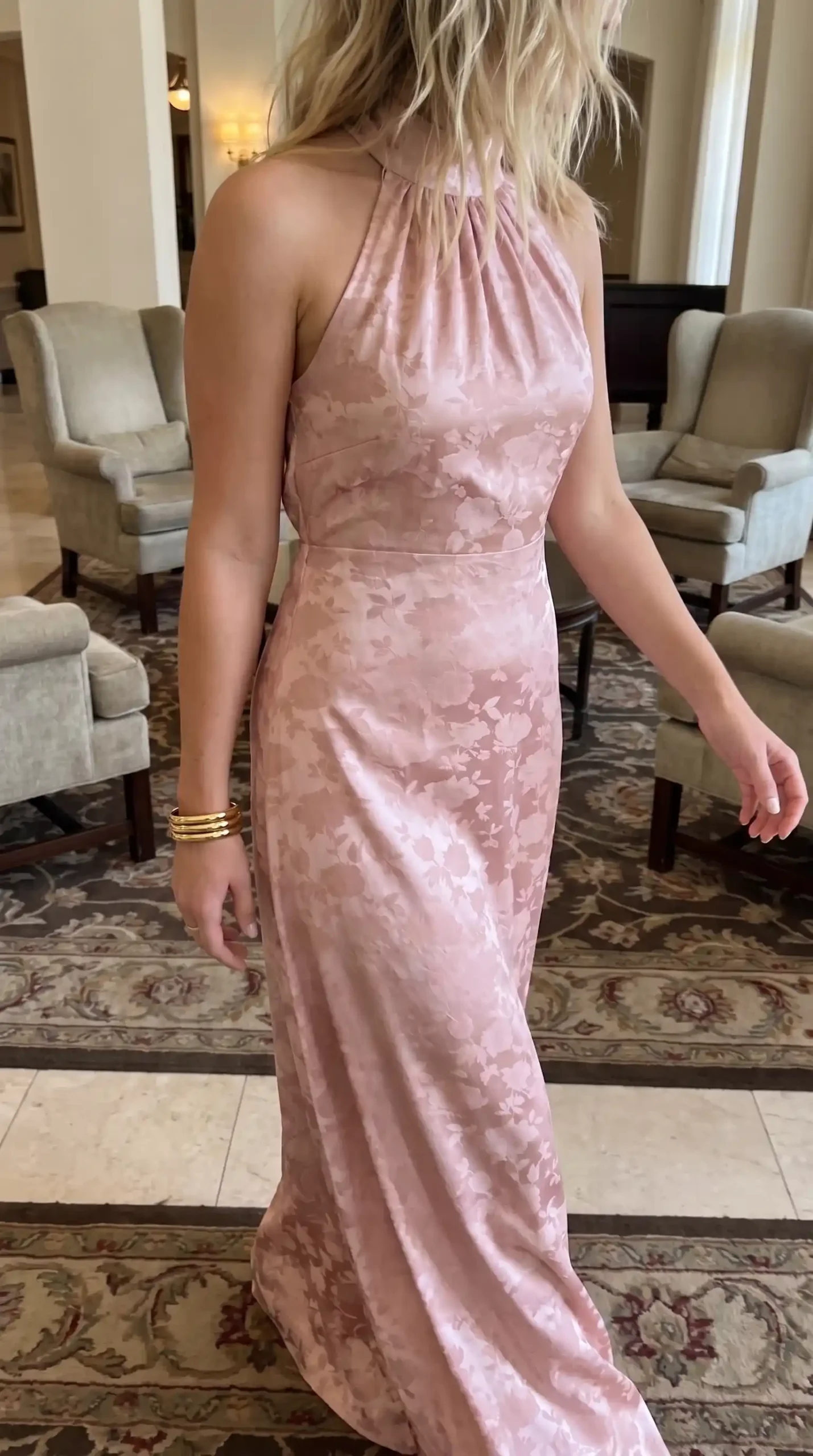Woman wearing dusty pink floral jacquard satin halter neck fitted maxi dress