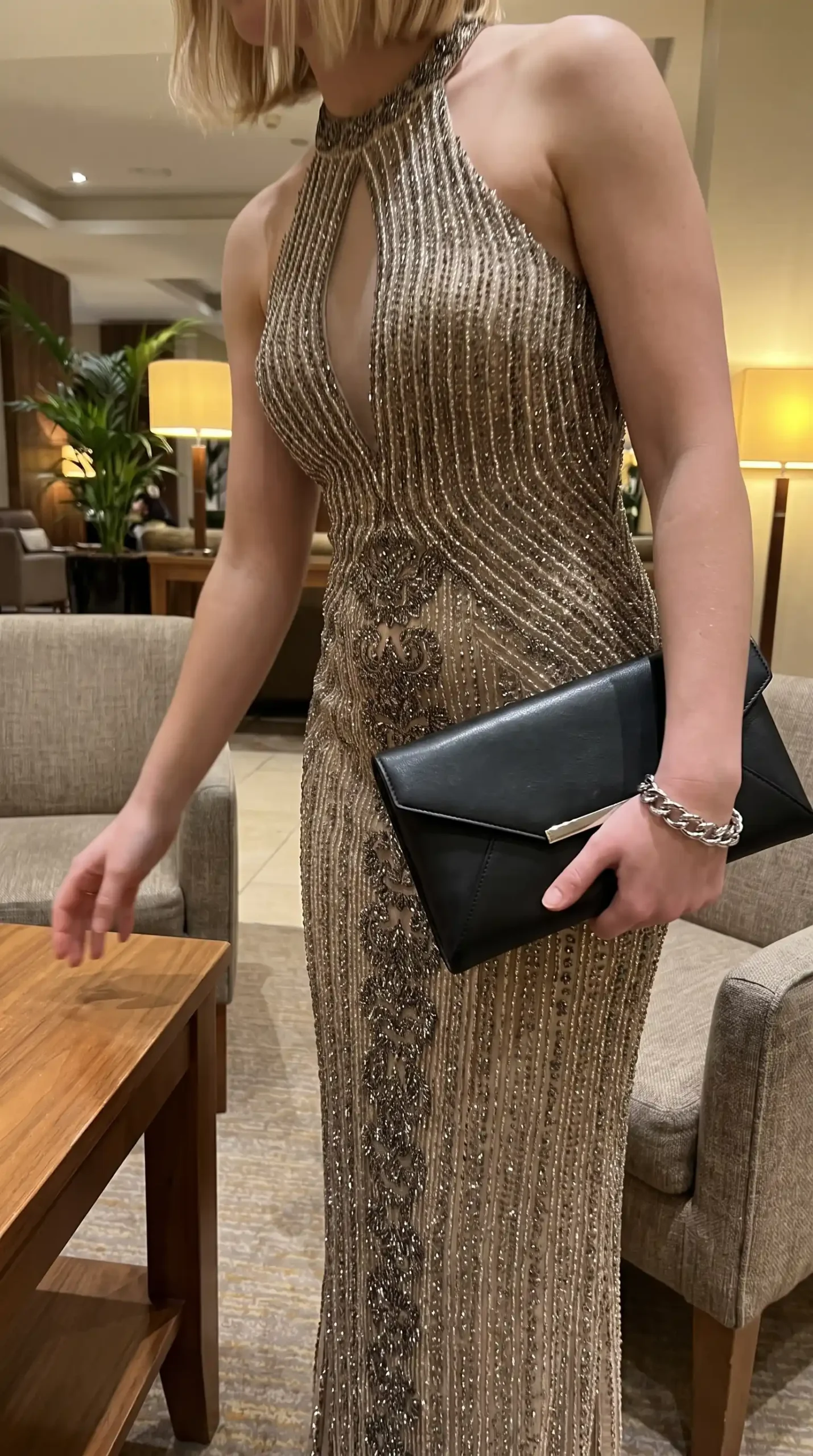 Woman wearing gold beaded embellished halter neck keyhole fitted maxi dress with black clutch