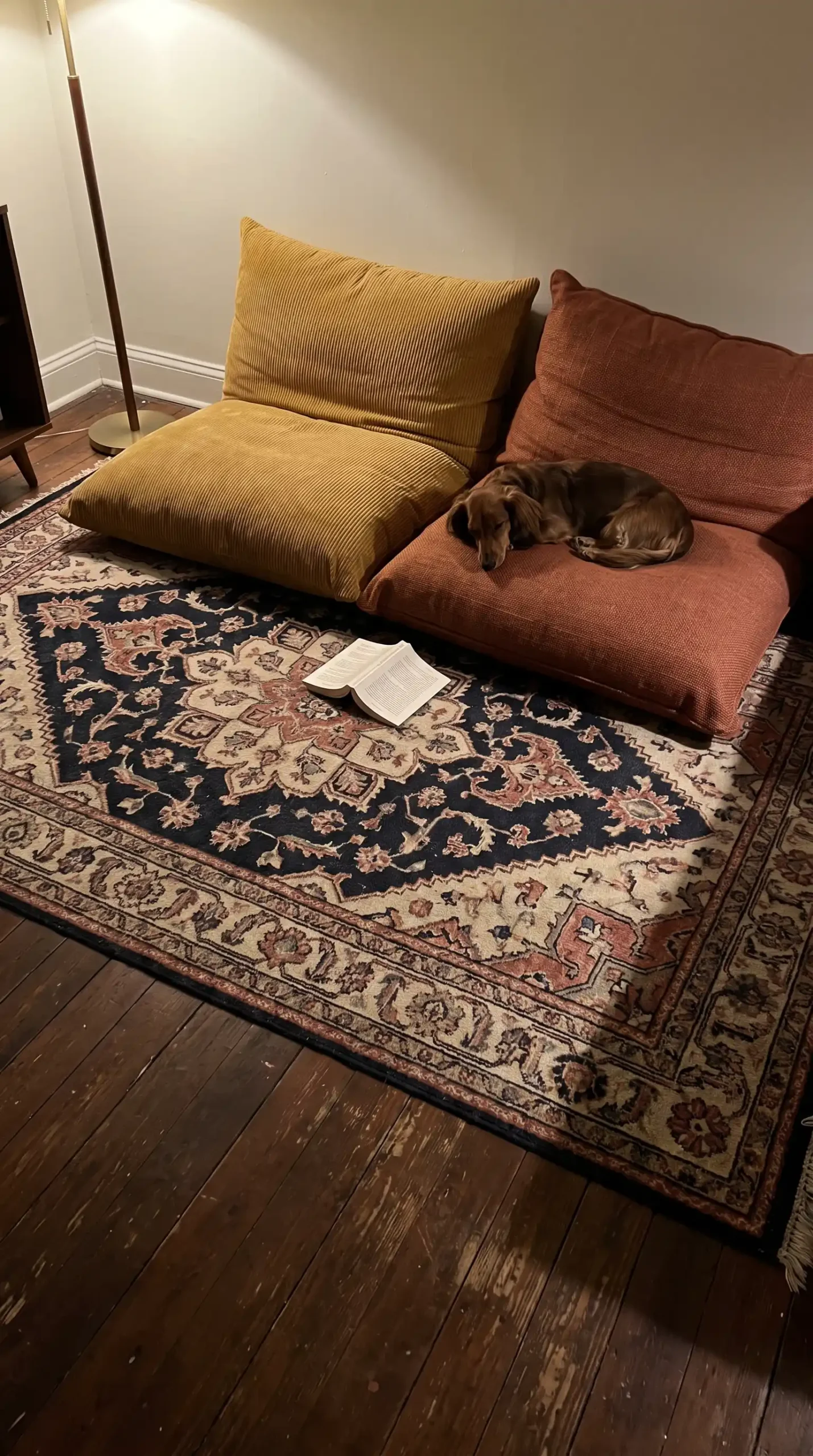 Dark navy kilim rug with mustard and rust floor cushions on dark hardwood eclectic living room floor