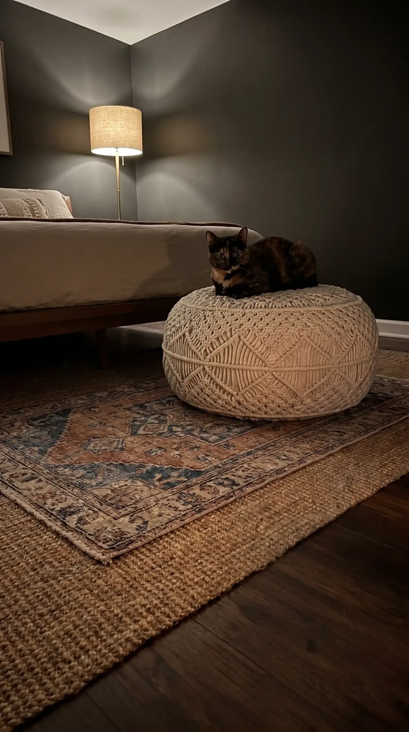 vintage Turkish rug in faded blue and rust over natural jute base rug in cozy boho bedroom floor with macrame pouf
