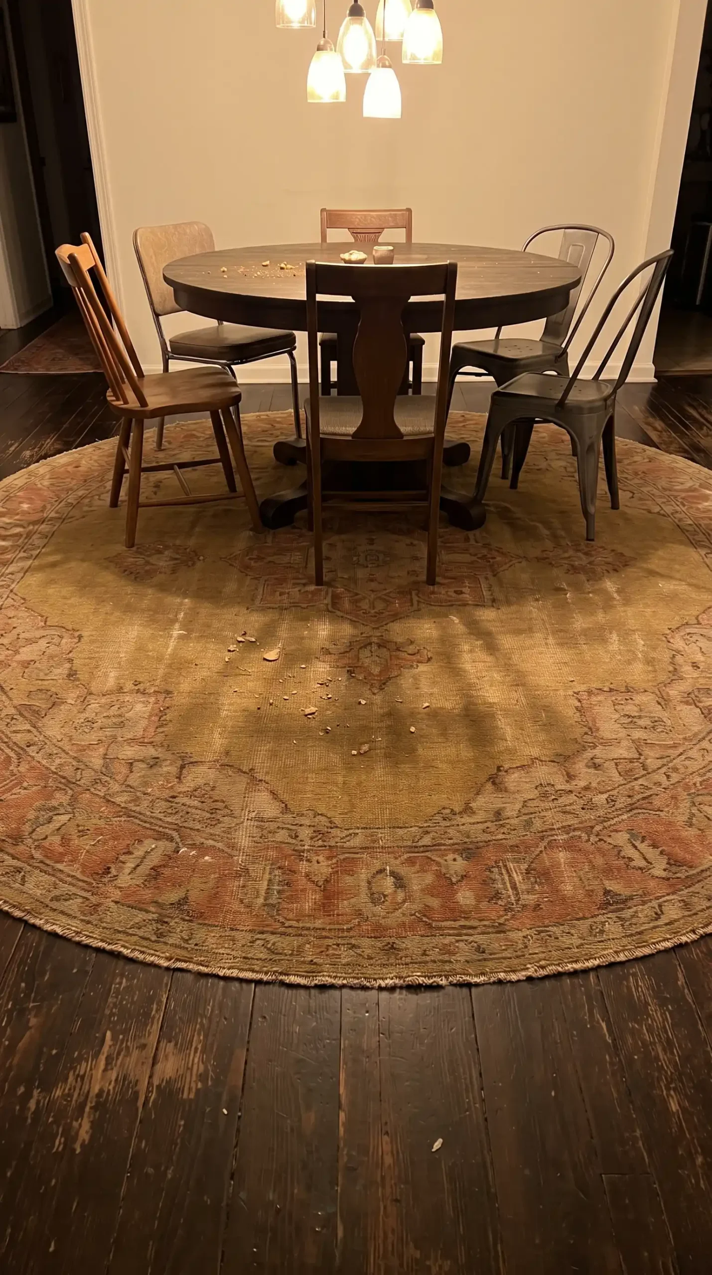 Large round faded mustard and terracotta hand knotted wool rug under dark wood round dining table in eclectic dining room