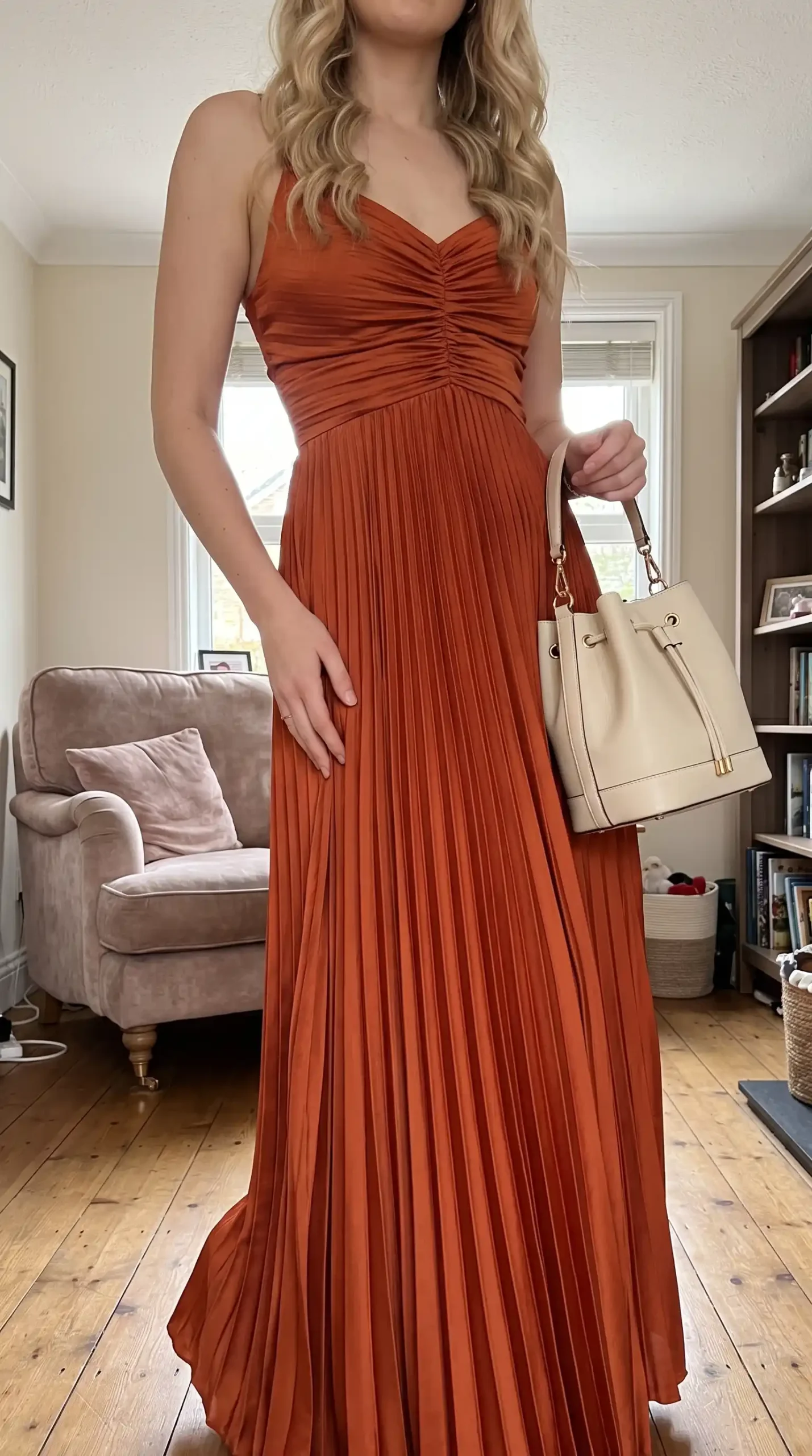 Woman wearing rust orange ruched sweetheart pleated maxi dress with cream bag
