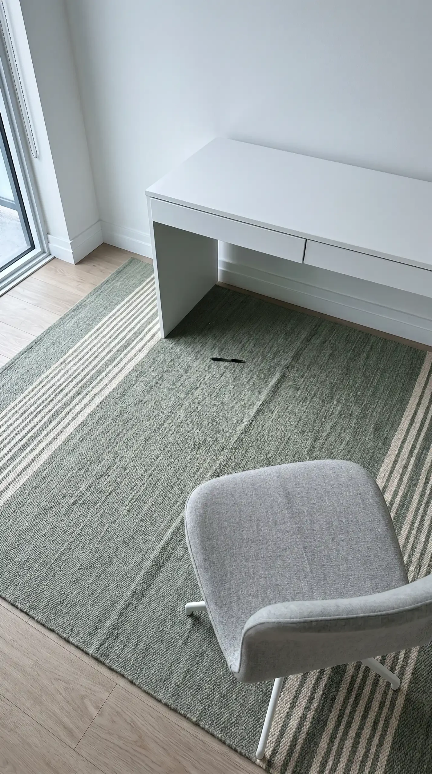 Large rectangular sage green and cream low pile wool rug under white floating desk in minimal home office