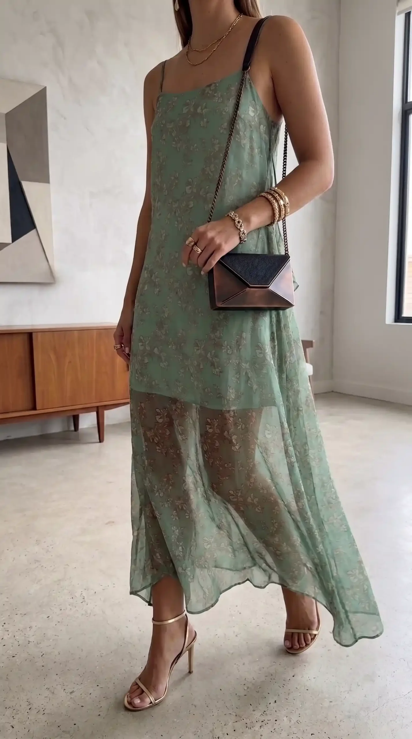 Woman wearing sage green sheer floral spaghetti strap maxi dress with gold heels and chain bag
