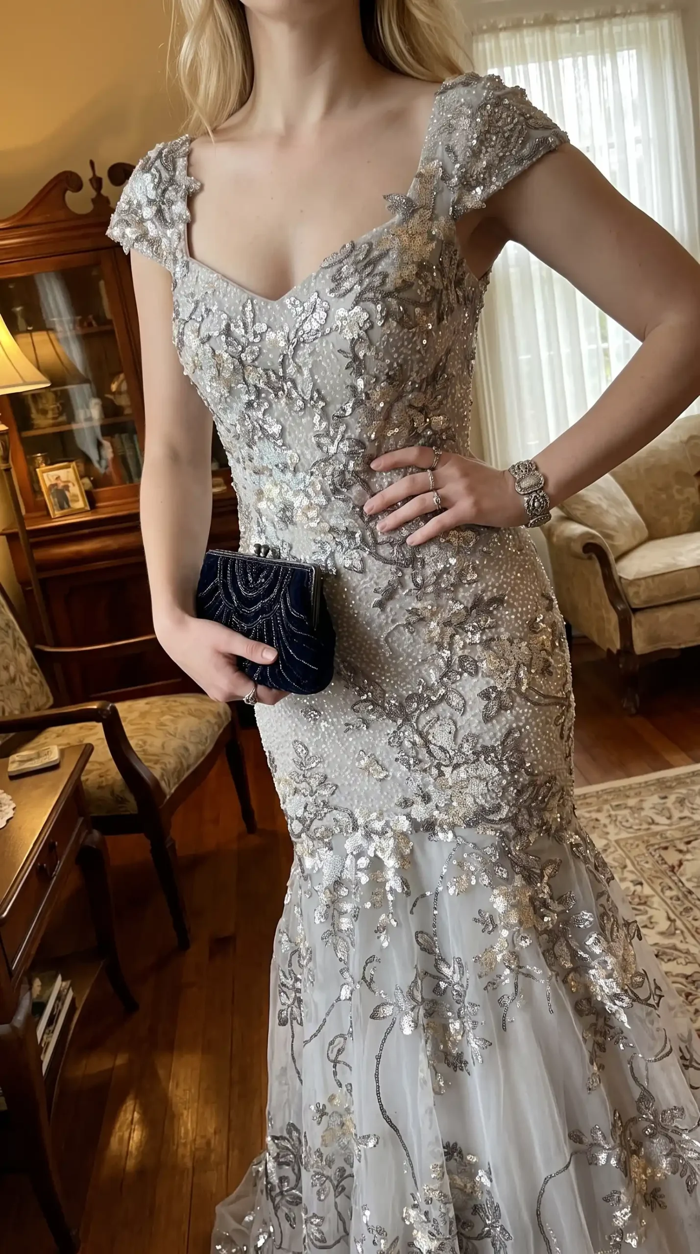 Woman wearing silver sequin floral beaded cap sleeve v neck mermaid maxi dress with navy clutch