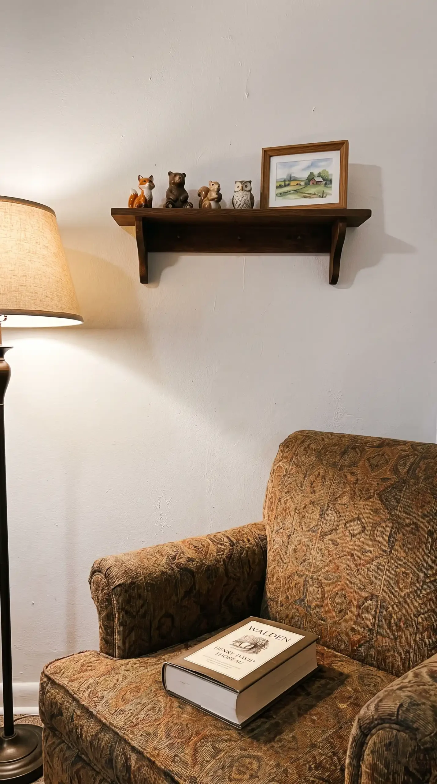Small wooden wall shelf with vintage ceramic figurines and tiny watercolour print in cozy reading corner
