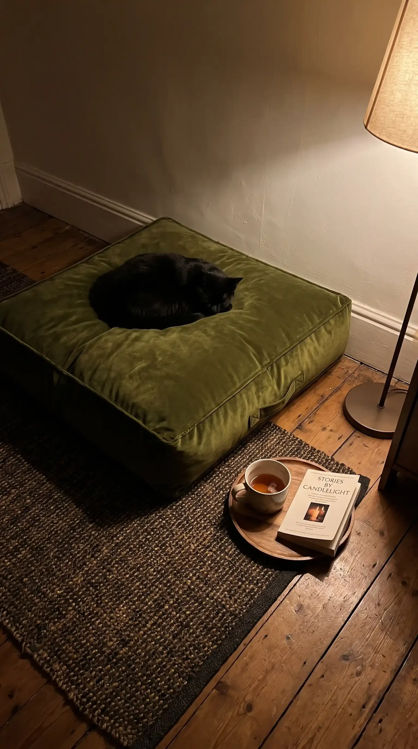Olive green velvet floor pouf on dark jute rug beside open book and tea cup in cozy reading nook