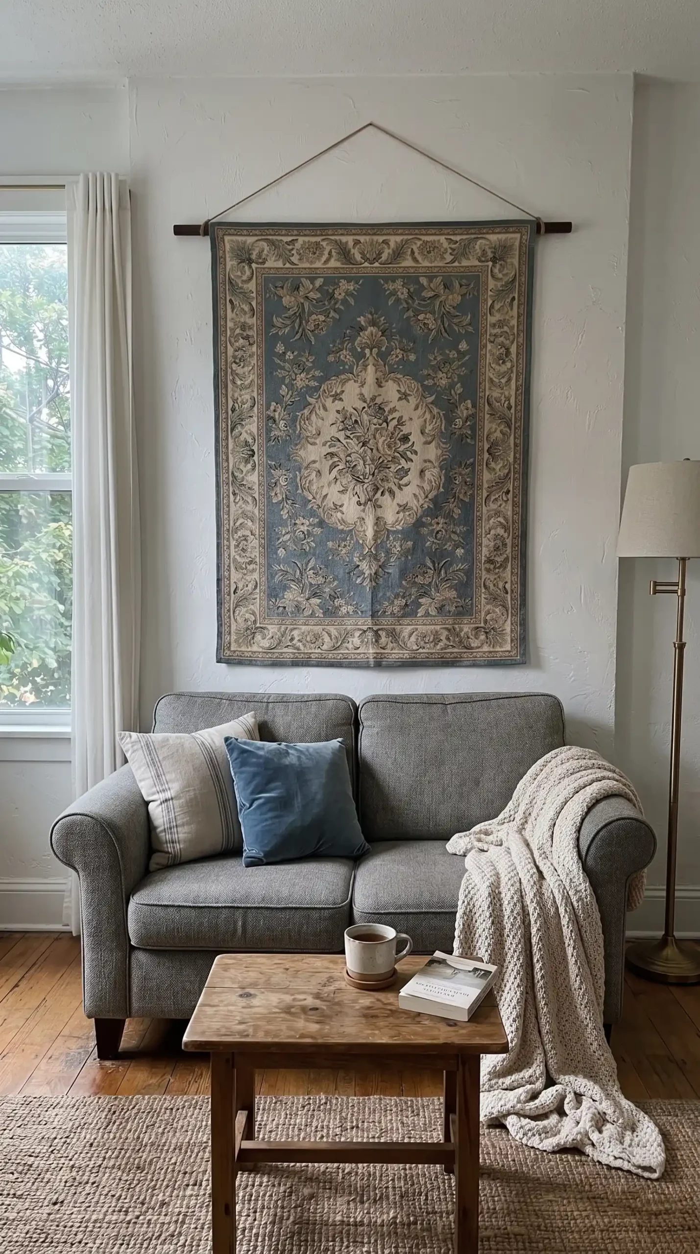 Large dusty blue and cream vintage floral tapestry hung on white wall behind small two seater sofa