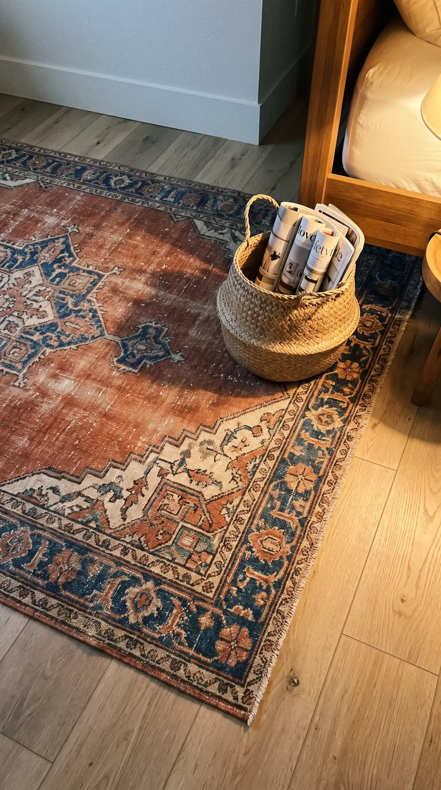 Faded terracotta and navy vintage Persian rug on light oak boho bedroom floor beside woven basket