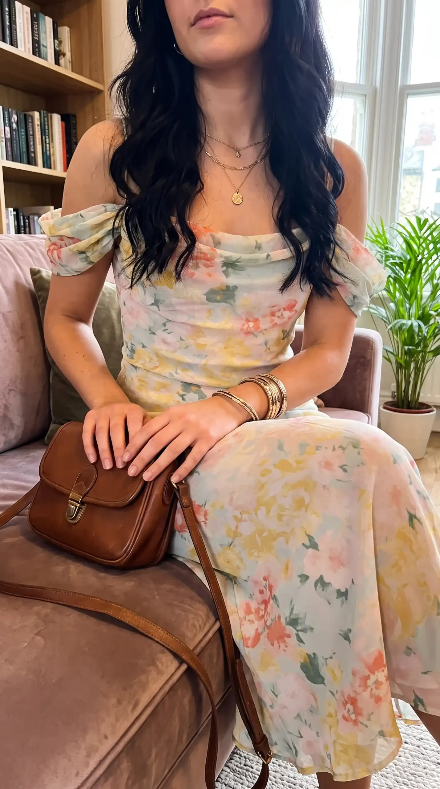 Woman sitting in white multicolor floral chiffon off shoulder puff sleeve maxi dress with tan bag